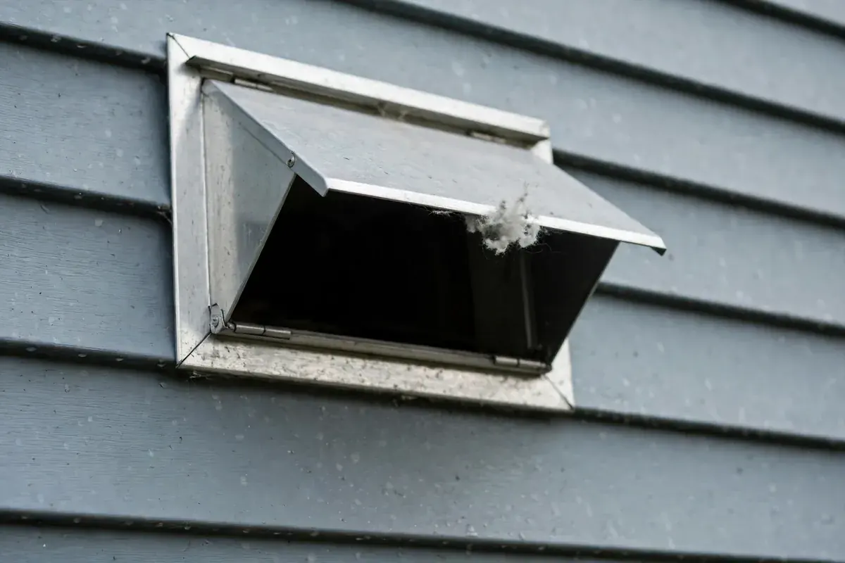 Dryer vent hood with the flap pushed open and lint stuck behind it