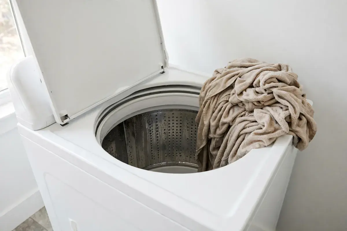 Top load washer lid open with a heavy lopsided clump of wet towels inside the tub